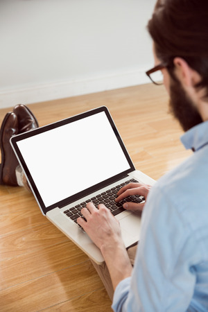 Handsome hipster using his laptop on wooden floorの写真素材