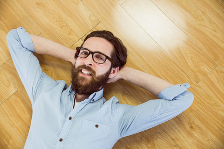 Handsome hipster lying and smiling on wooden floorの写真素材