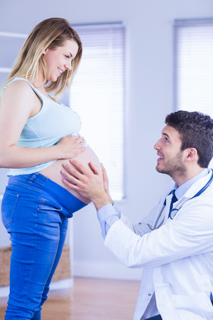 Smiling doctor checking stomach of standing pregnant patient in medical officeの写真素材