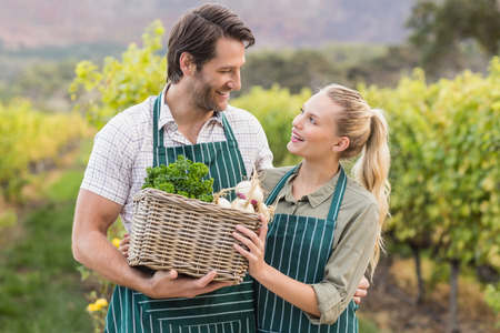 Two young happy farmers holding a basket of vegetables in the fieldsの写真素材