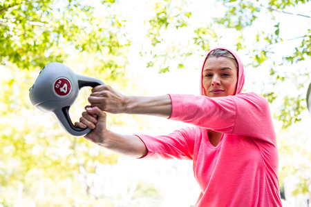 A pretty woman in a pink outfit doing exercise with a weight on a sunny day