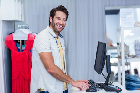 Portrait of smiling cashier typing in clothing store