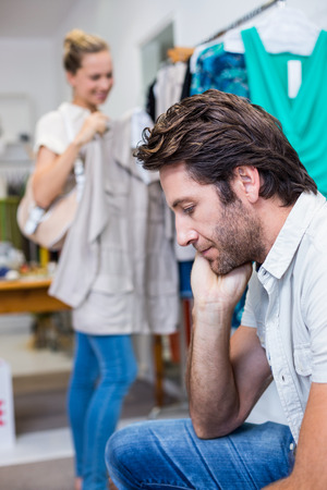 Bored man sitting in front of his girlfriend in clothing storeの写真素材