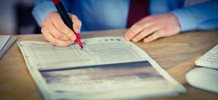 Businessman marking the newspaper with marker in his office
