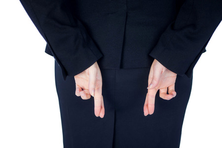 Close up pretty businesswoman with finger crossed against a white wallの写真素材