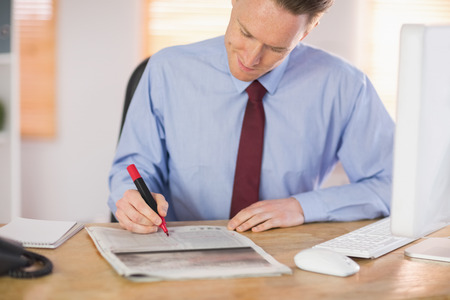 Businessman marking the newspaper with marker in his officeの写真素材