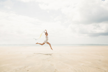 Stylish woman leaping with scarf at the beachの写真素材