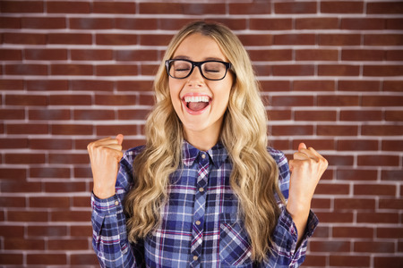 Gorgeous blonde hipster celebrating success against red brick backgroundの写真素材