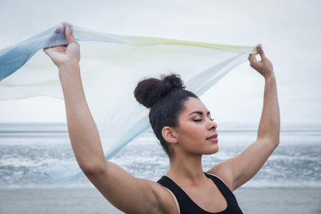 Fit girl standing with scarf blowing in wind at the beachの写真素材