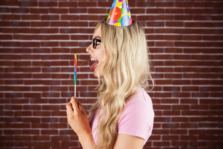 A beautiful hipster with party hat holding a giant lollipop against a red brick wallの写真素材