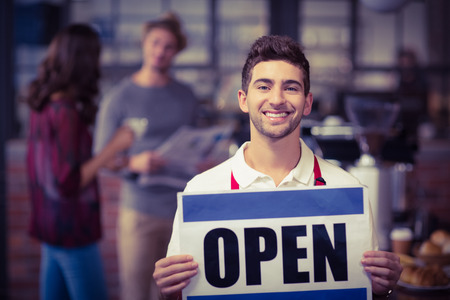 Portrait of a waiter posing with open sign at the coffee shop