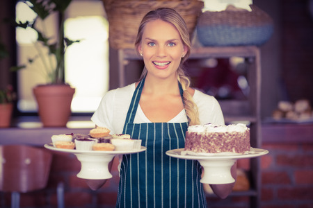 Waitress holding a chocolate cake and cupcakes at the coffee shopの写真素材