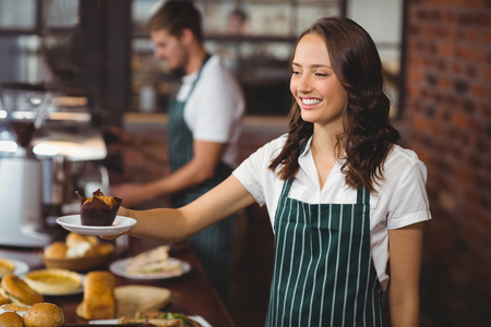 Smiling waitress serving a muffin at the coffee shopの写真素材