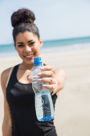 Fit woman showing water bottle at the beachの写真素材