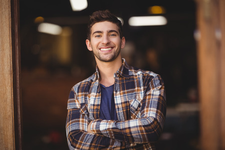 Portrait of smiling casual waiter with arms crossed at coffee shopの写真素材