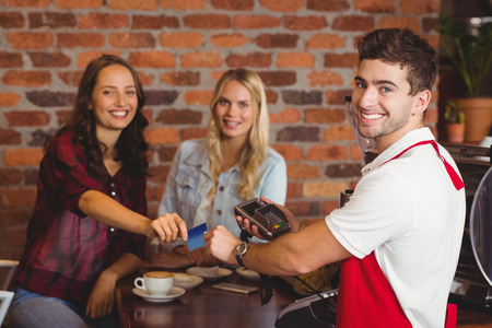 Portrait of friends handing a credit card at the coffee shopの写真素材
