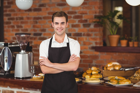 Portrait of smiling barista in front of counter with arms crossed at coffee shopの写真素材
