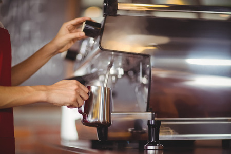 Barista steaming milk at the coffee machine at the coffee shopの写真素材