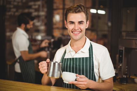 Portrait of a barista pouring milk in a cup at the coffee shopの写真素材
