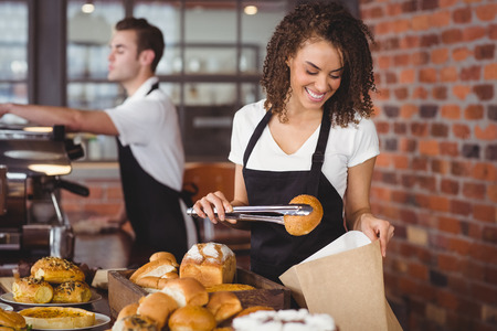 Smiling waitress putting bread roll in paper bag at coffee shop