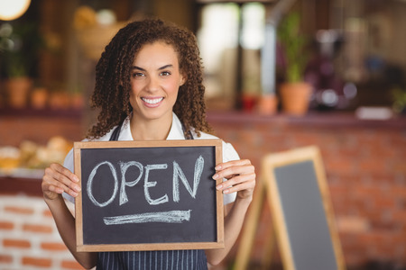 Portrait of a waitress showing chalkboard with open sign at the coffee shop