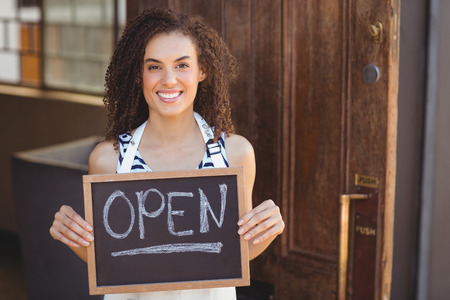 Portrait of waitress showing chalkboard with open sign at coffee shopの写真素材