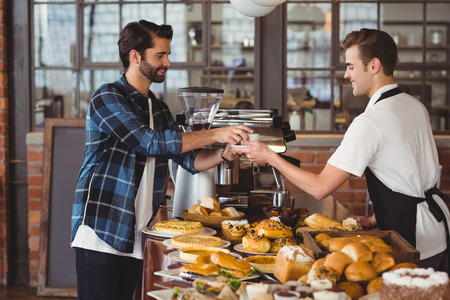 Smiling hipster getting cup of coffee from barista at coffee shopの写真素材