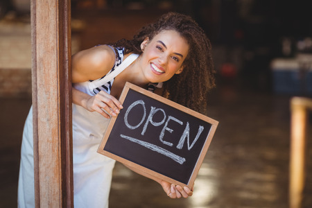 Portrait of waitress showing chalkboard with open sign at coffee shopの写真素材