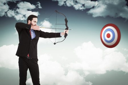 Focused businessman shooting a bow and arrow against blue skyの写真素材