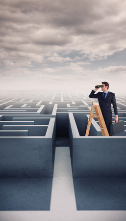 Businessman looking on a ladder against cloudy sky over mazeの写真素材