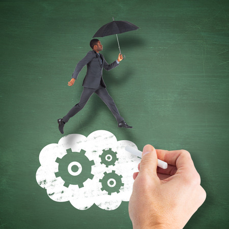 Businessman walking and holding umbrella against green chalkboardの写真素材