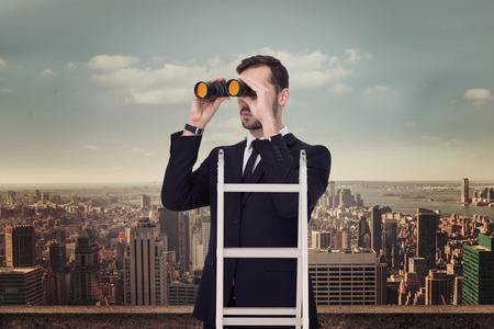 Businessman looking on a ladder against balcony overlooking cityの写真素材