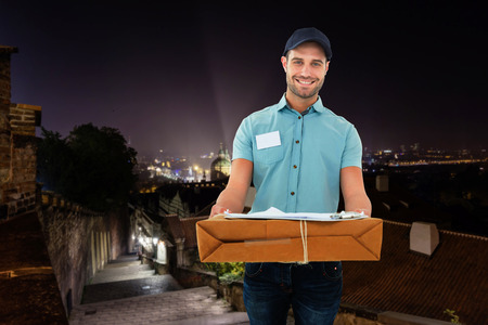 Handsome courier man with parcel against cityscape by nightの写真素材