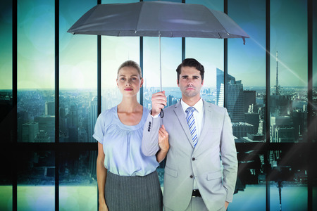 Business people holding a black umbrella against room with large window looking on cityの写真素材