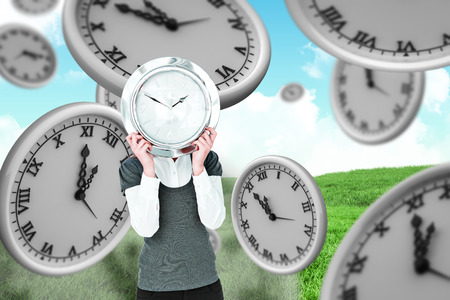 Woman holding clock in front of her head  against green field under blue sky