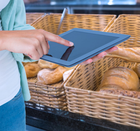 Woman using tablet pc  against baskets with breads freshly baked and tongsの写真素材