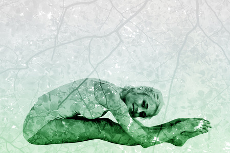 Toned woman doing the paschimottanasana pose against branches and leavesの写真素材