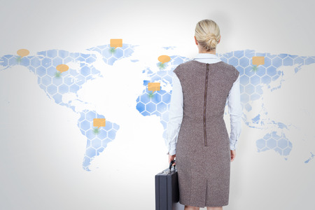 Back turned businesswoman holding a briefcase against world mapの写真素材