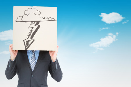 Businessman hiding head with a box against blue skyの写真素材