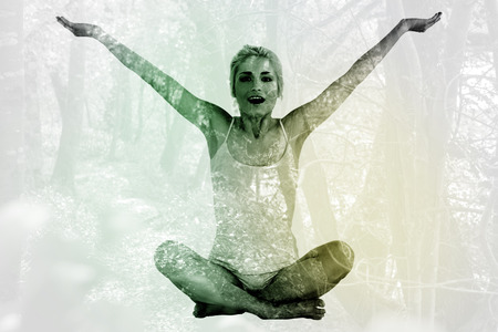 Toned young woman sitting with arms outstretched against tranquil autumn scene in forestの写真素材