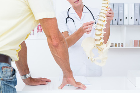 Doctor showing her patient a spine model in medical officeの写真素材