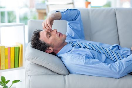 Worried businessman with head in hands lying on couch in living room