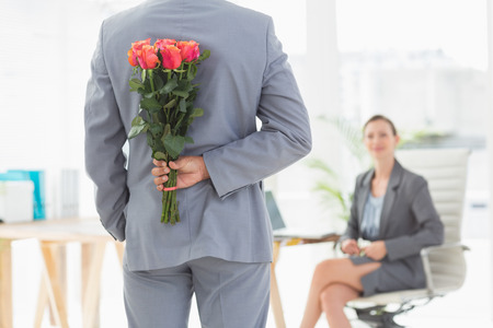 Businessman holding flowers behind his back in an officeの写真素材