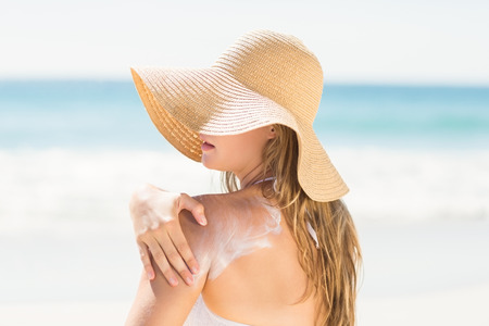 Pretty blonde woman spreading sun tan lotion on her shoulder at the beachの写真素材