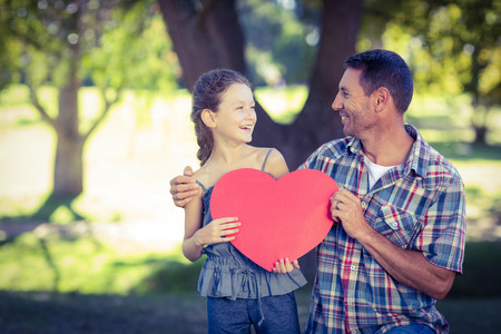 Father and daughter holding a heart in the park on a sunny dayの写真素材
