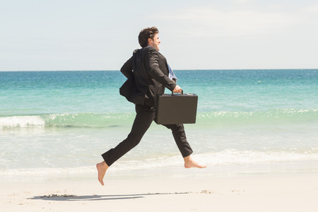 Businessman jumping in front of the sea at the beachの写真素材