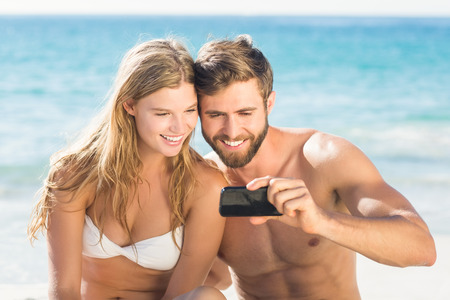 Happy couple looking at smartphone at the beachの写真素材