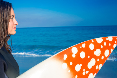 Woman in wetsuit with a surfboard on a sunny day at the beachの写真素材
