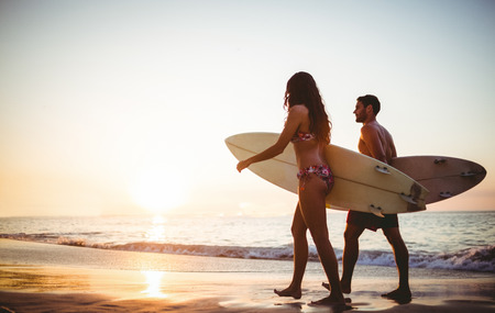 Couple holding surfboards looking at ocean at the beachの写真素材
