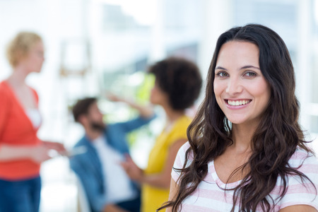 Portrait of smiling young businesswoman with colleagues in background at the officeの写真素材
